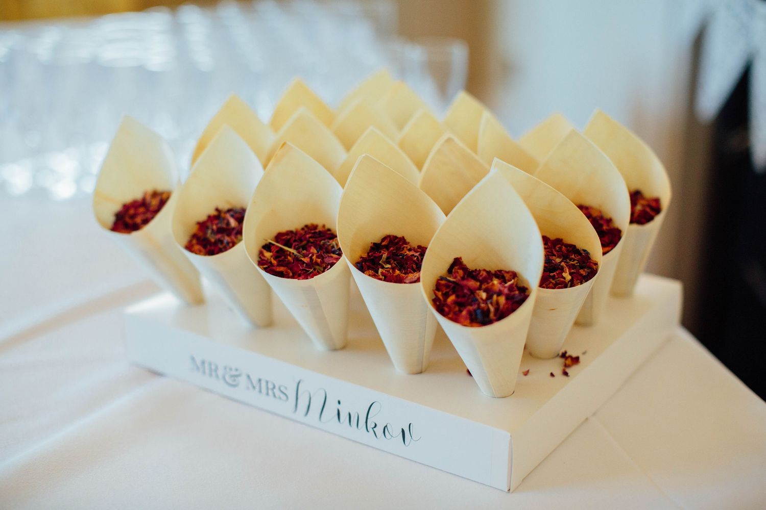 White paper cones filled with red flower petals arranged in display holder for wedding ceremony.