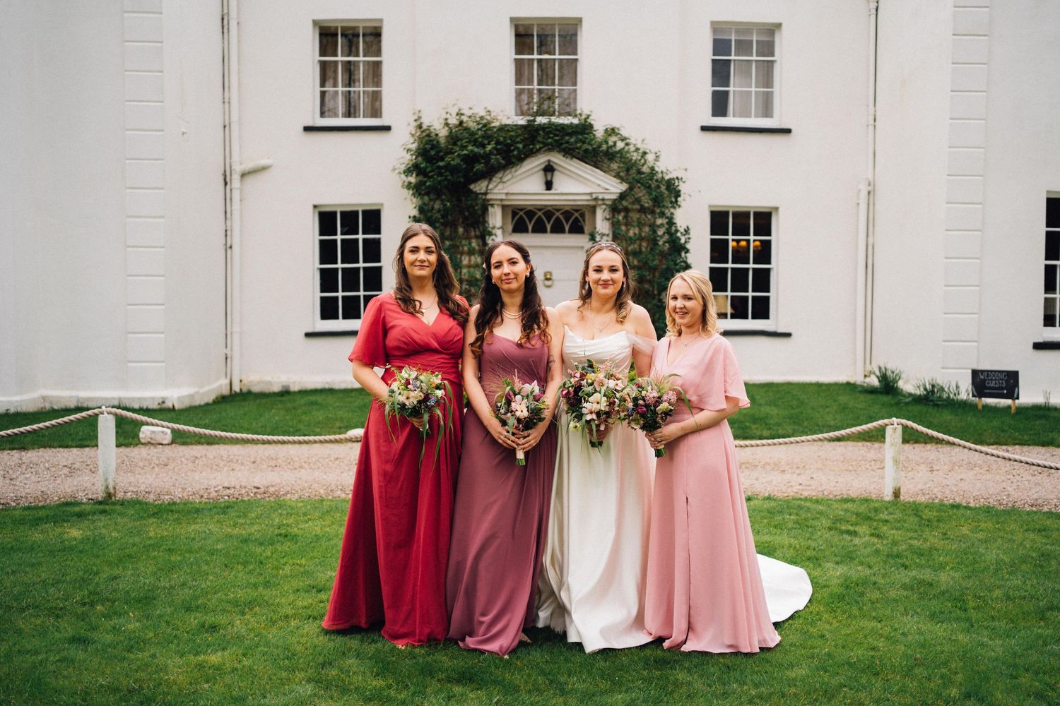 A group of people in formal attire gather for wedding photos in front of a white historic building.