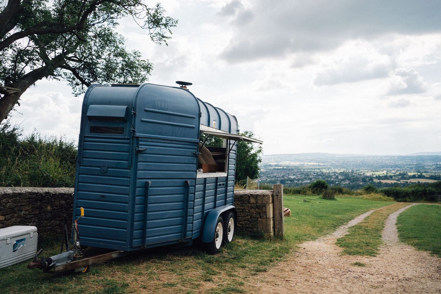 Blue storage containers and trailers positioned along a rural dirt path with rolling hills in background.