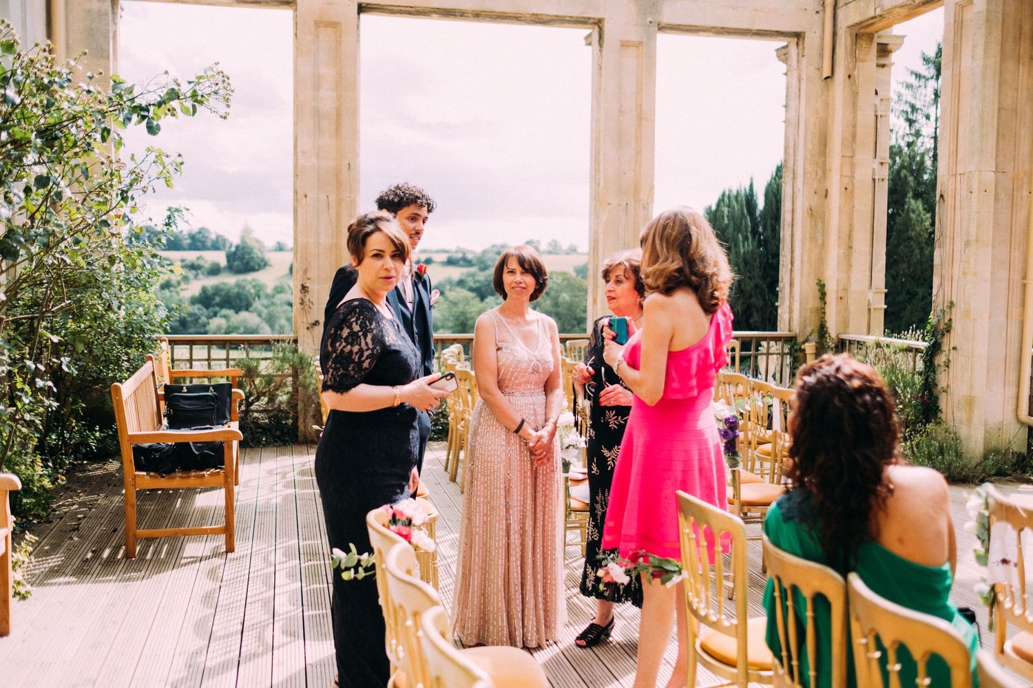 Wedding guests gather on an elegant columned terrace overlooking a scenic coastal view during a daytime celebration.