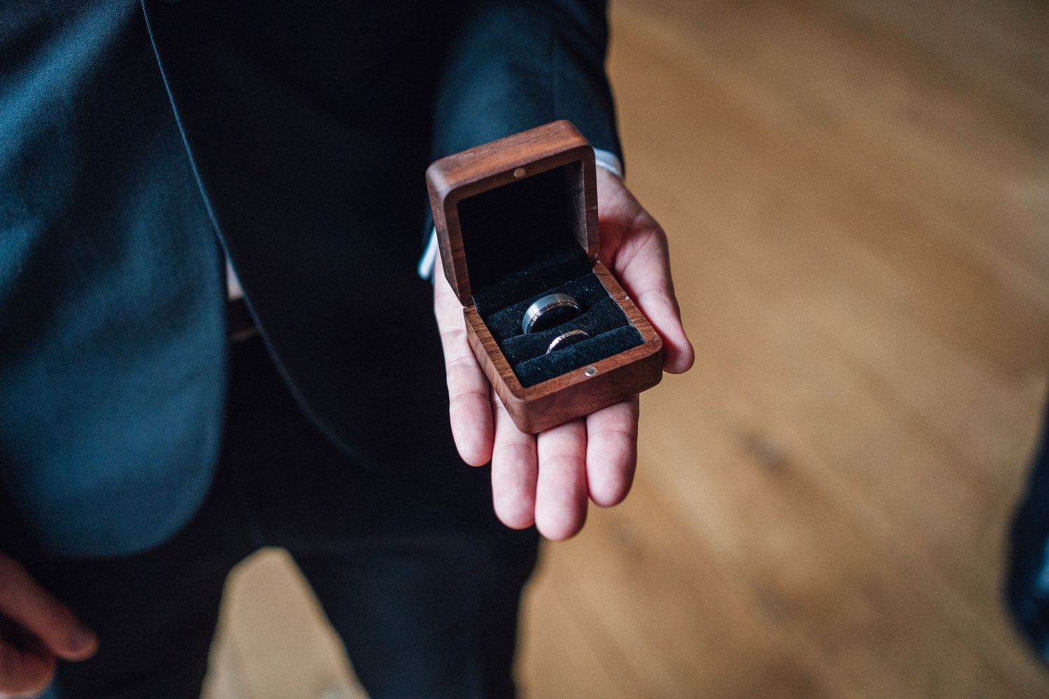 Close-up details of hands exchanging rings during an intimate wedding ceremony on wooden flooring.