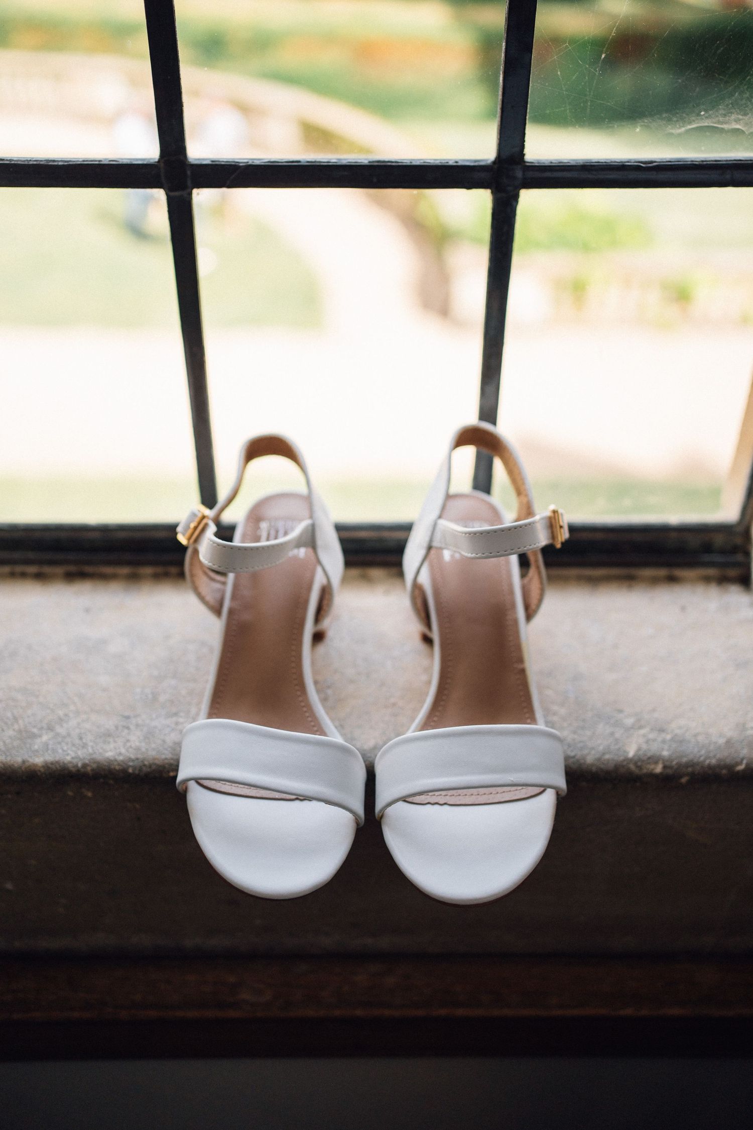 White bridal sandals displayed on a windowsill with natural lighting.
