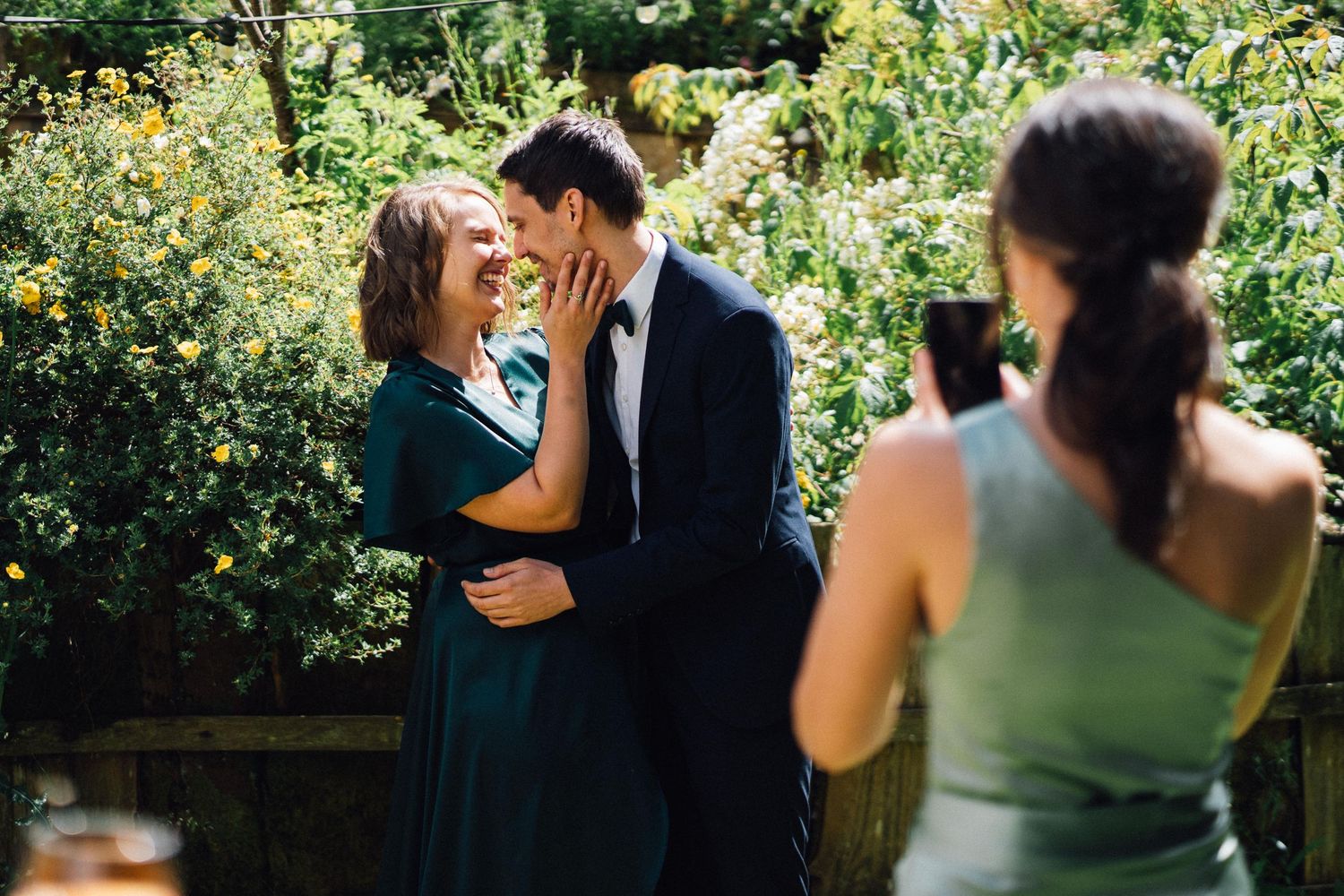 Couple embraces in a lush green garden setting during an outdoor celebration.