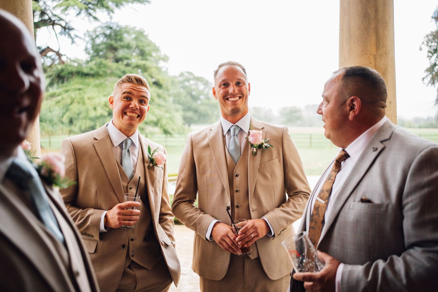 Groomsmen in tan suits sharing laughs during outdoor wedding photos.