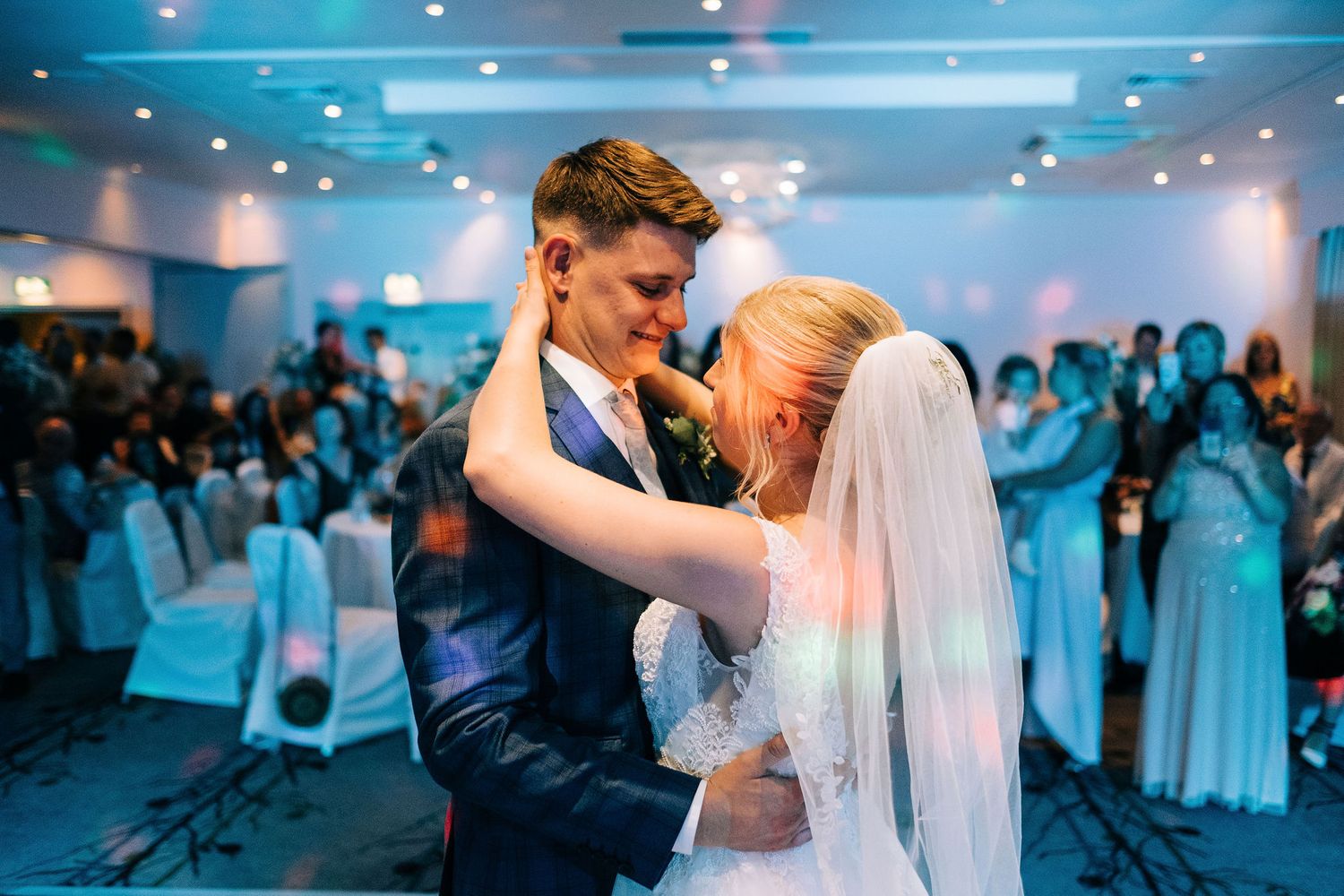 Couple shares their first dance under blue lighting at an elegant wedding reception.
