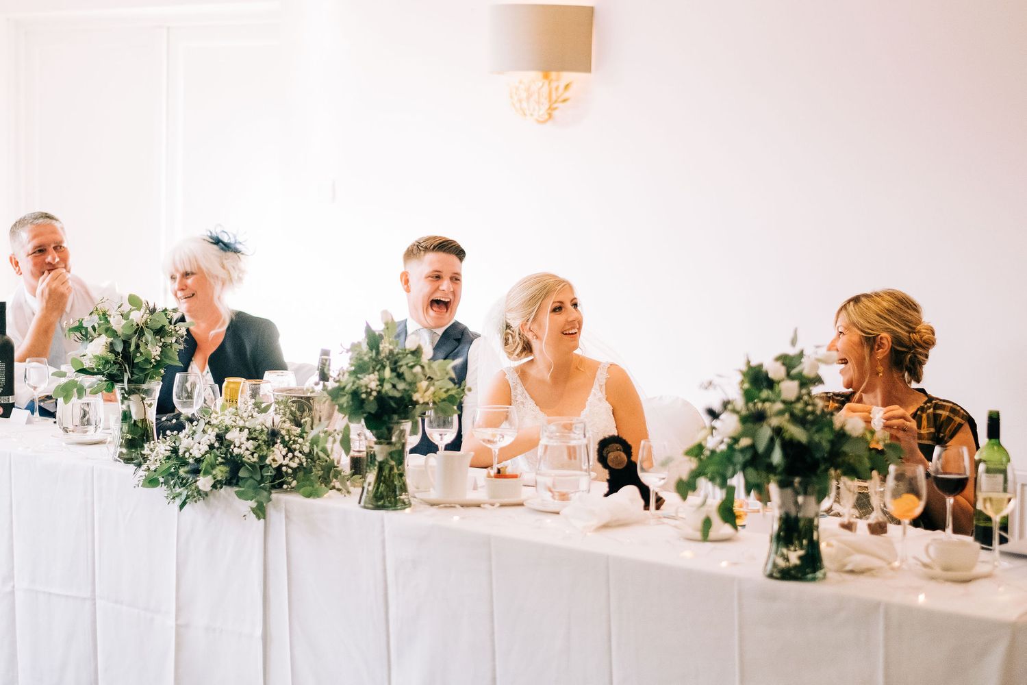 Elegant white wedding reception table decorated with floral centerpieces and glowing ambient lighting.