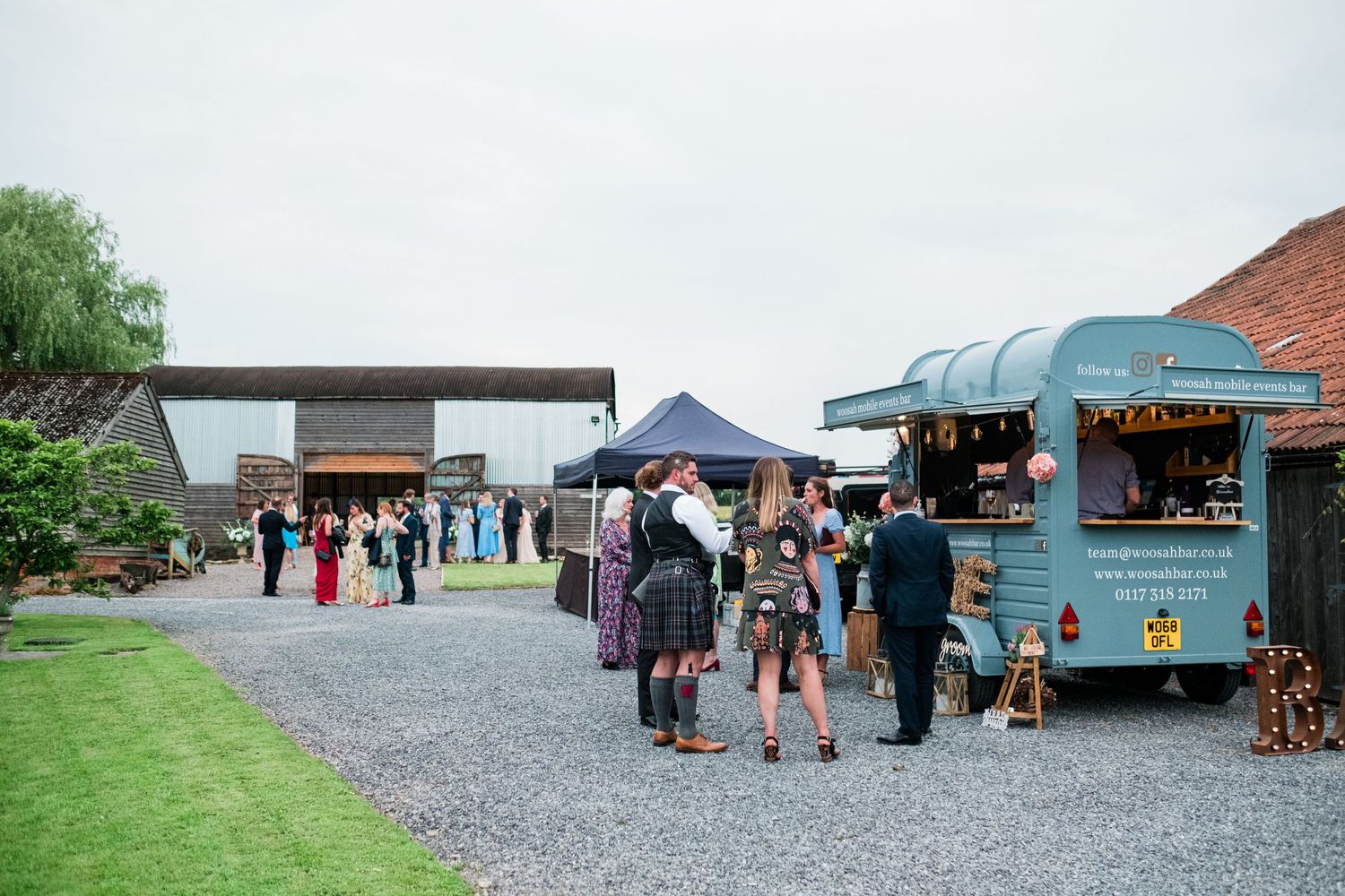 Outdoor wedding venue with food trucks and guests mingling on gravel path.