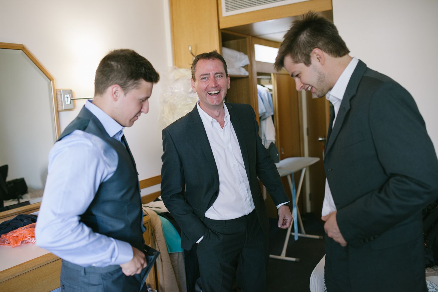 Groomsmen laughing and joking while getting dressed for wedding.