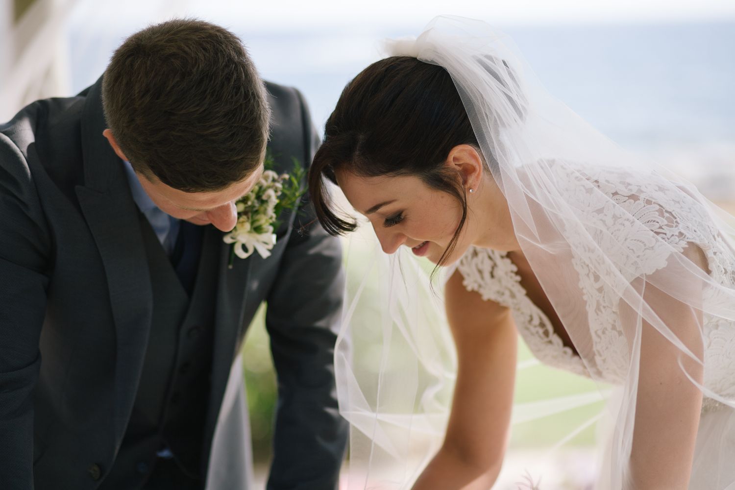A tender moment between a bride in a lace veil and groom in a dark suit during their outdoor wedding ceremony.