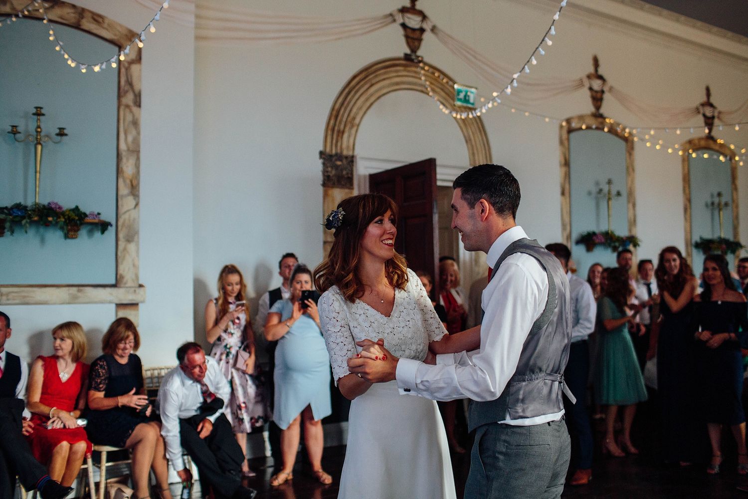 Couple dancing in an elegant blue-decorated room with string lights and watching guests.