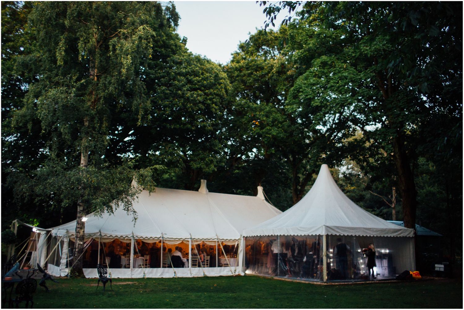 Row of white wedding marquees set up in a lush green garden setting.