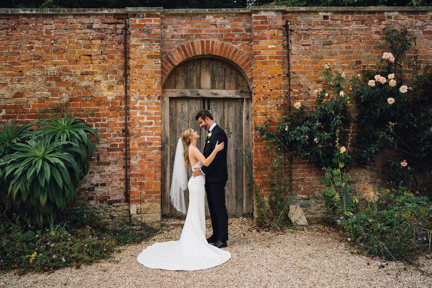 Romantic wedding portraits captured against historic brick wall and garden setting.