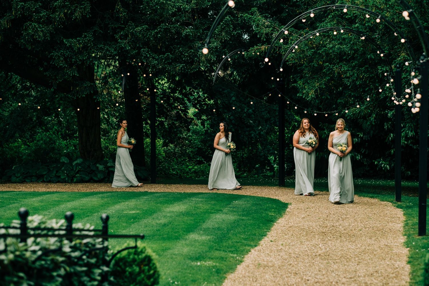 Wedding party members in matching gray dresses stand spaced apart on a manicured lawn.