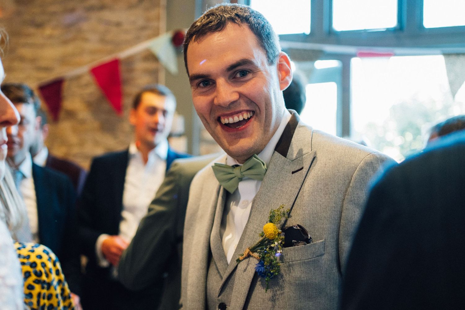 Wedding guests share joyful laughter and conversation during an indoor reception with exposed brick walls.