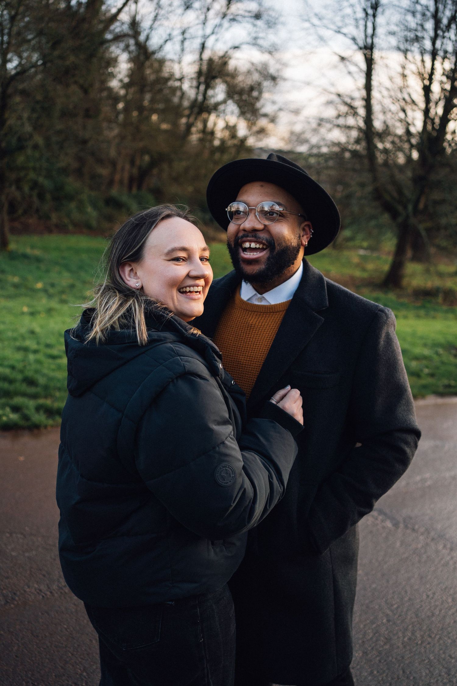 A couple shares joyful laughter together during an outdoor photoshoot in a park setting.