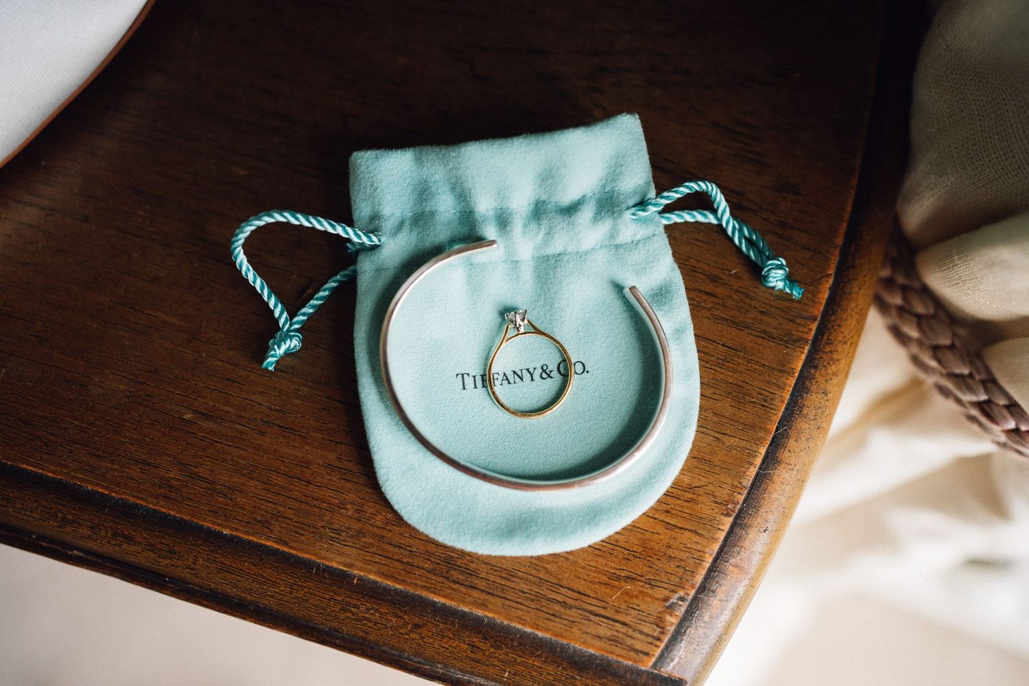Wedding ring displayed on a ceramic dish with turquoise drawstring pouch on wooden surface.