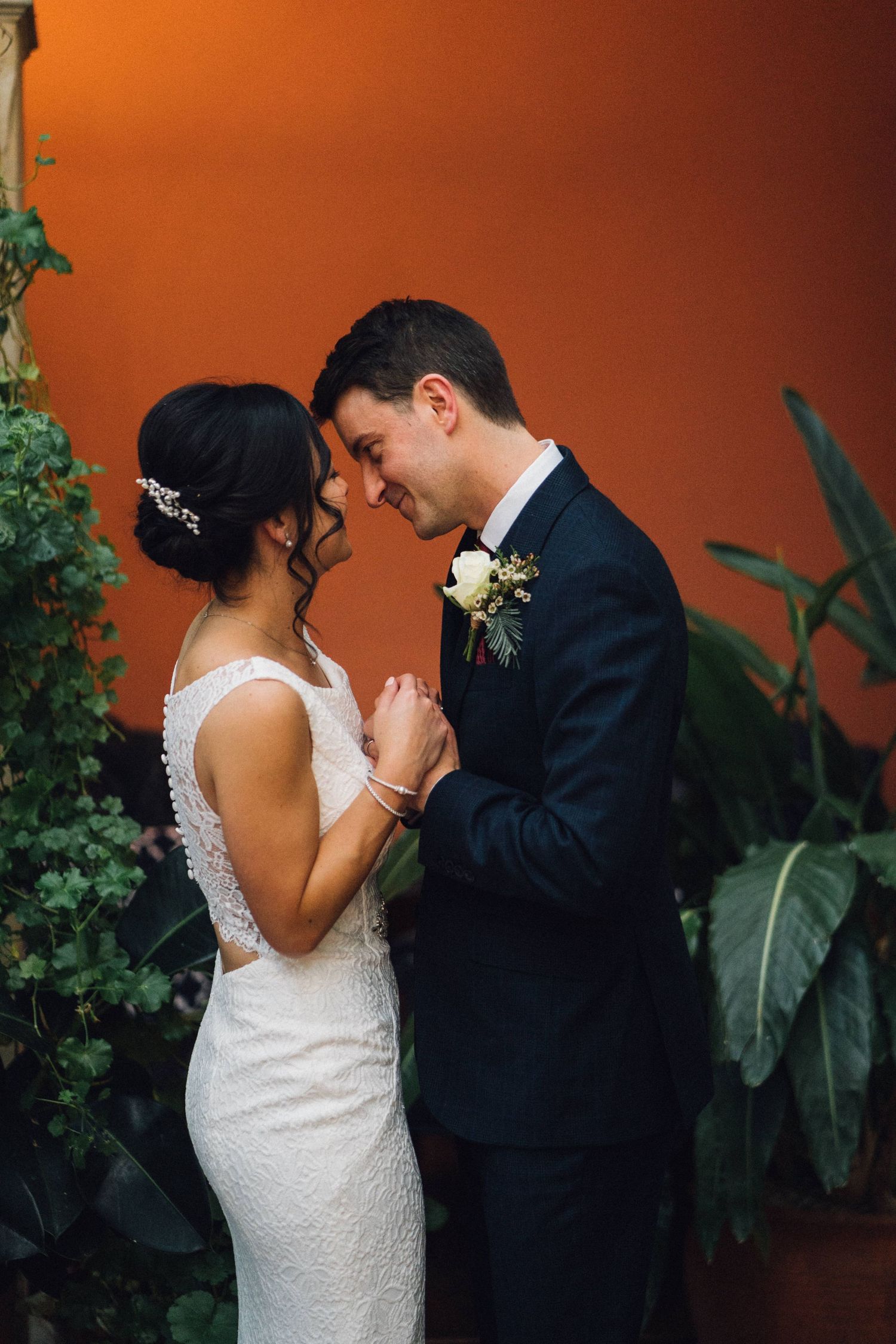 Intimate wedding moment shared against vibrant orange walls and tropical plants.