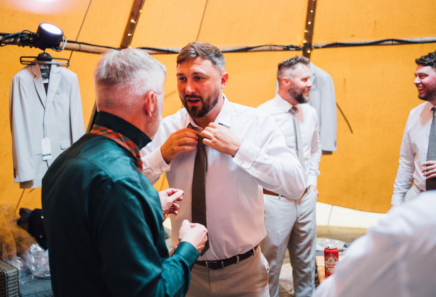Men getting ready in orange-tinted tipi with formal wear hanging in background.
