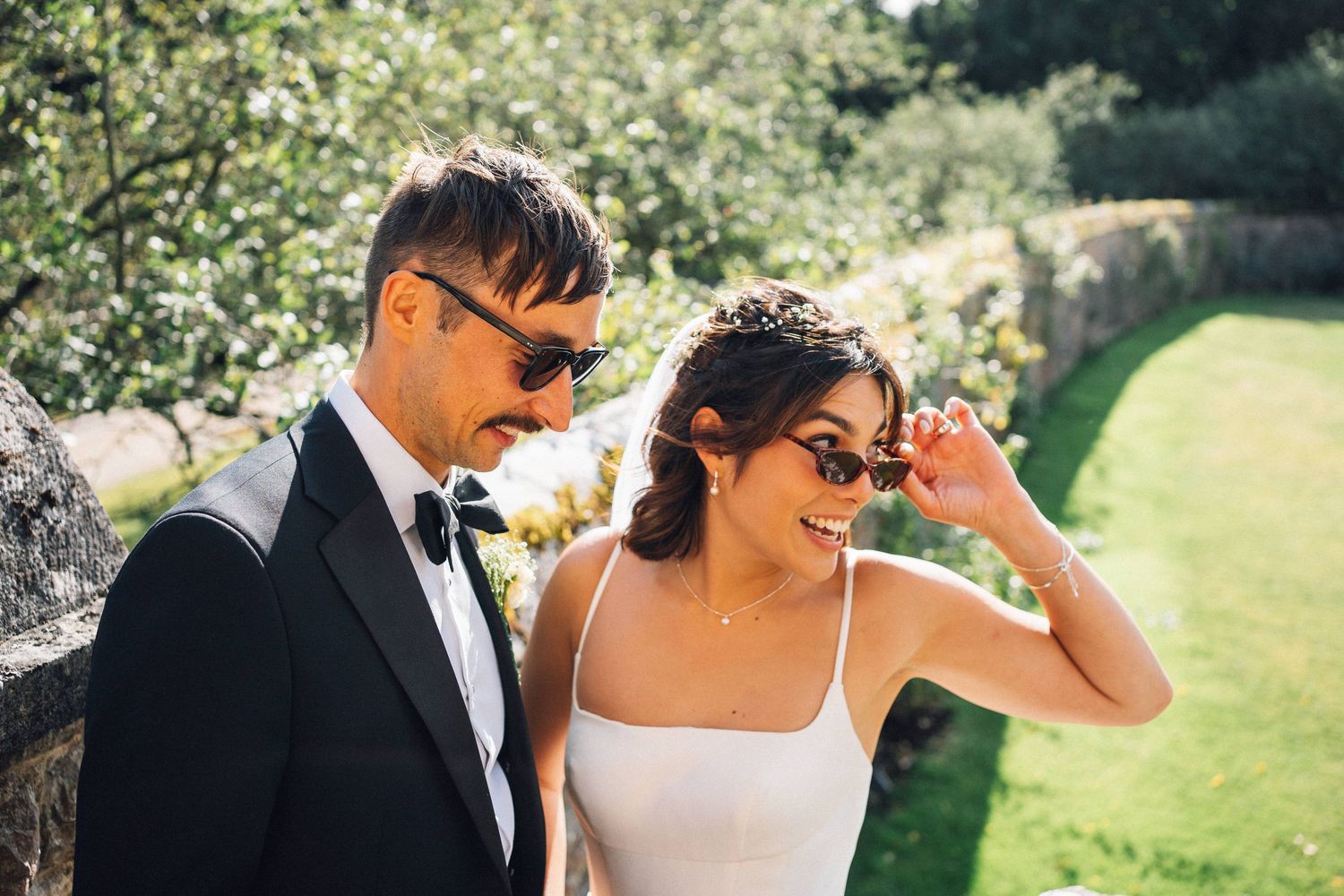 Joyful wedding couple wearing sunglasses share a candid moment outdoors.