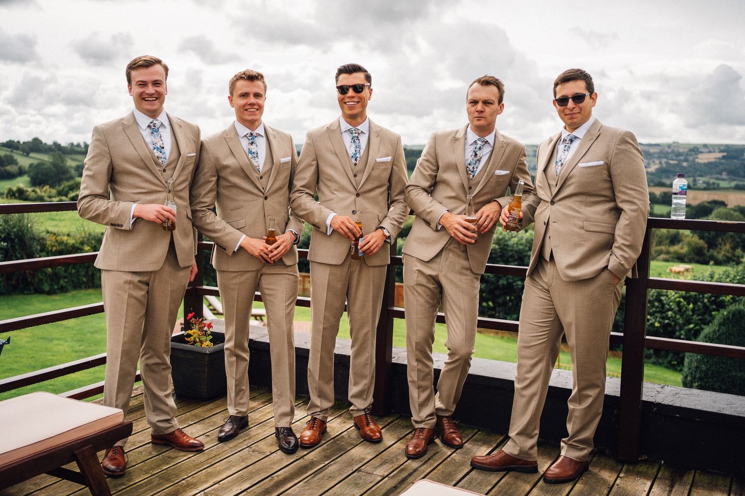 Groomsmen in tan suits and blue ties pose together on a balcony.