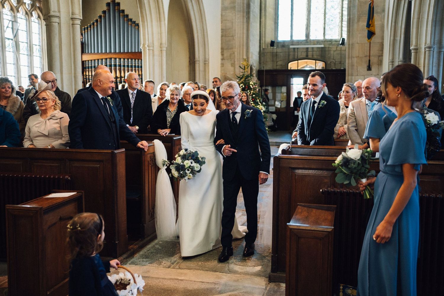 Wedding guests gather in a church aisle during a ceremony while standing and watching the proceedings.