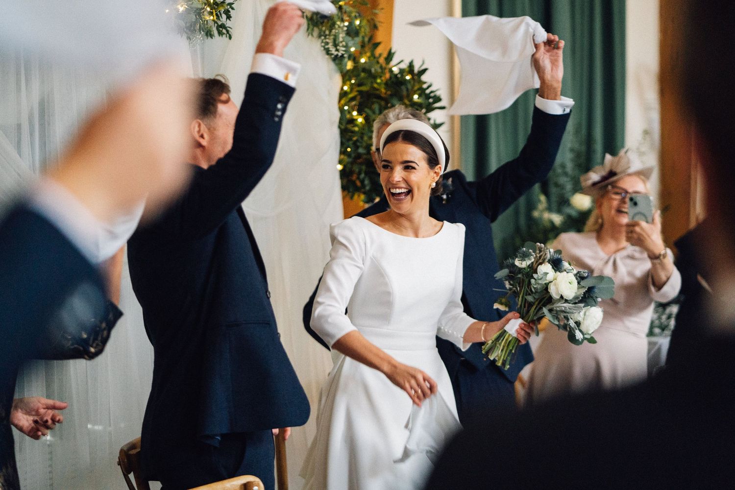 Wedding guests dancing and celebrating at an elegant indoor reception venue with festive decorations.