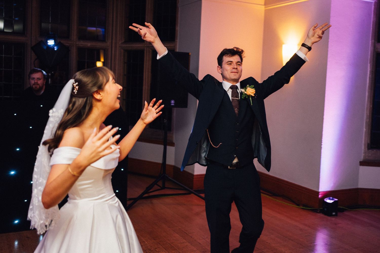 A joyful couple dances enthusiastically during their wedding reception with arms raised.