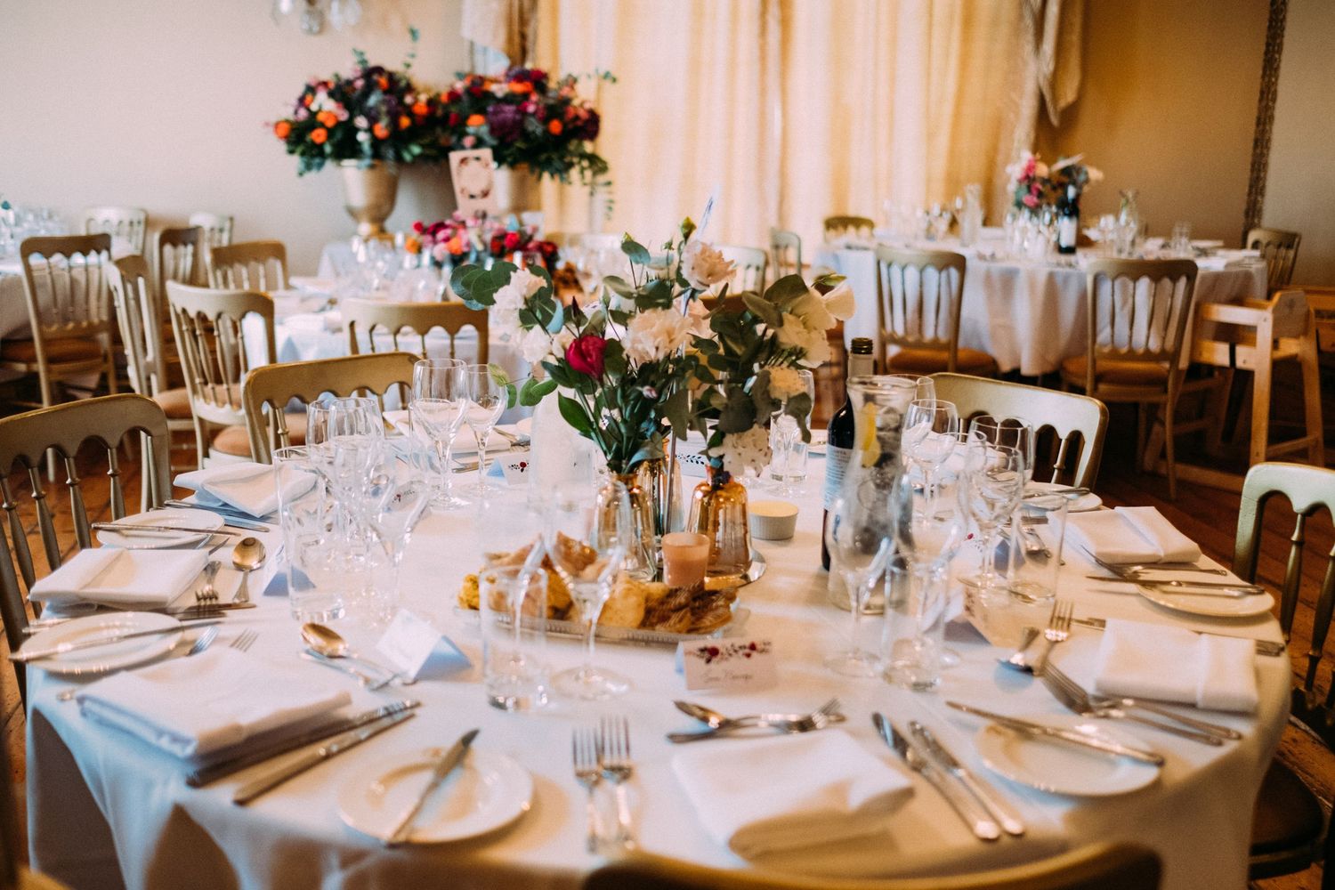Elegant wedding reception tables set with white linens, floral centerpieces and glowing candles in a banquet hall.
