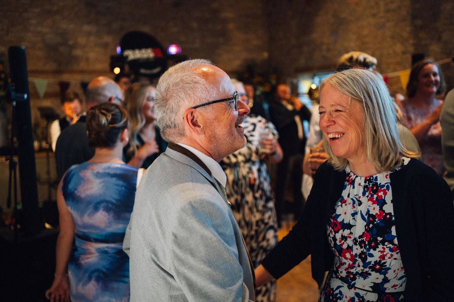 Wedding guests dancing and celebrating in a rustic stone venue with atmospheric lighting.