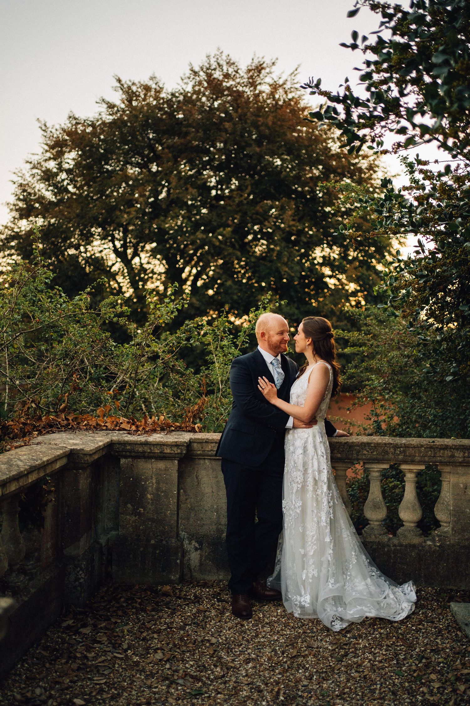 Newlyweds pose for romantic portraits on stone terrace surrounded by autumn foliage.