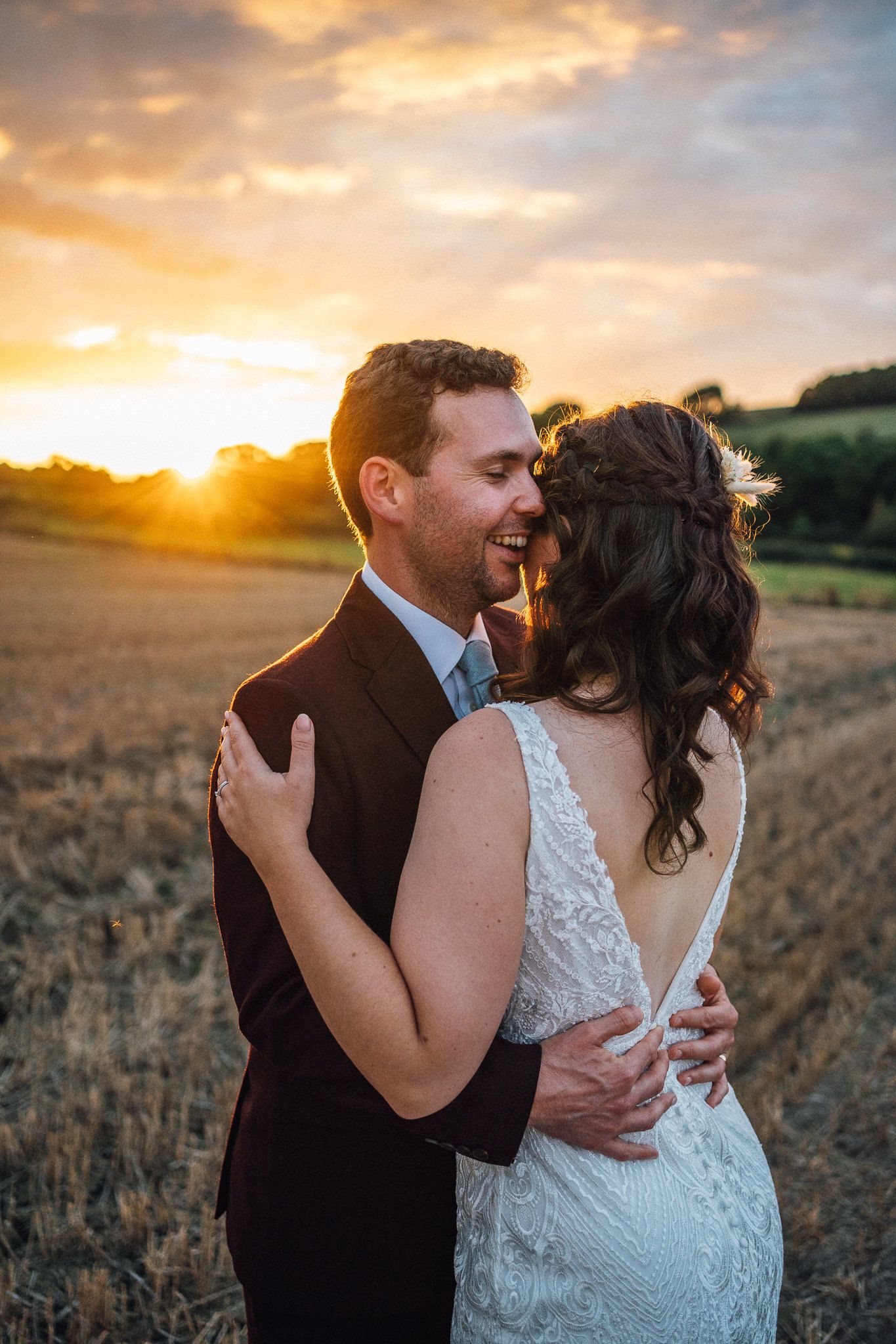 Romantic couple embraces in a golden wheat field at sunset during their rustic outdoor wedding photoshoot.