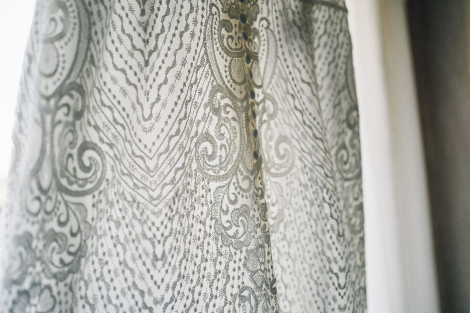 Delicate white lace curtain with intricate floral patterns and swirling designs hangs in soft natural light.