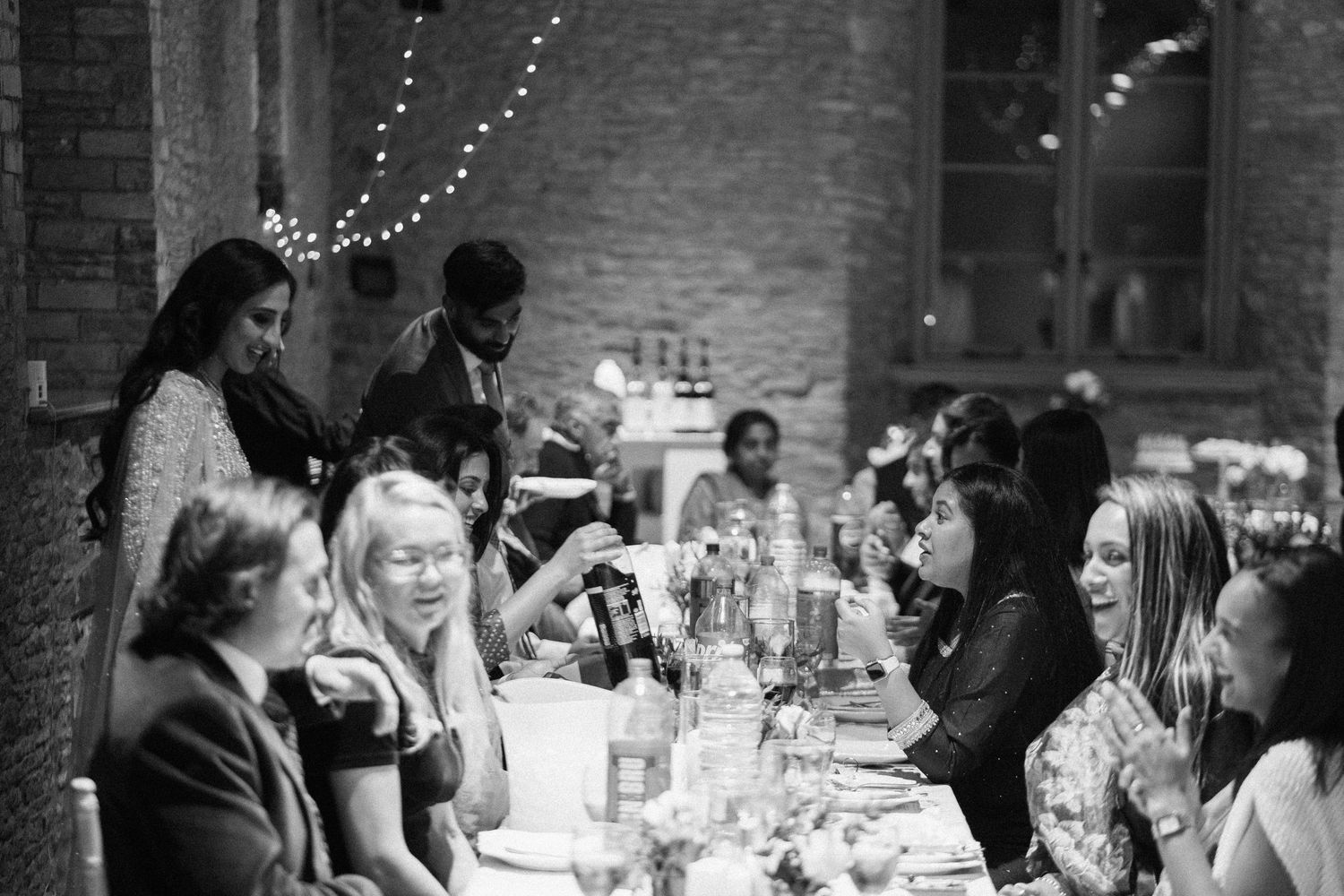 Black and white photo of wedding guests socializing at reception tables.