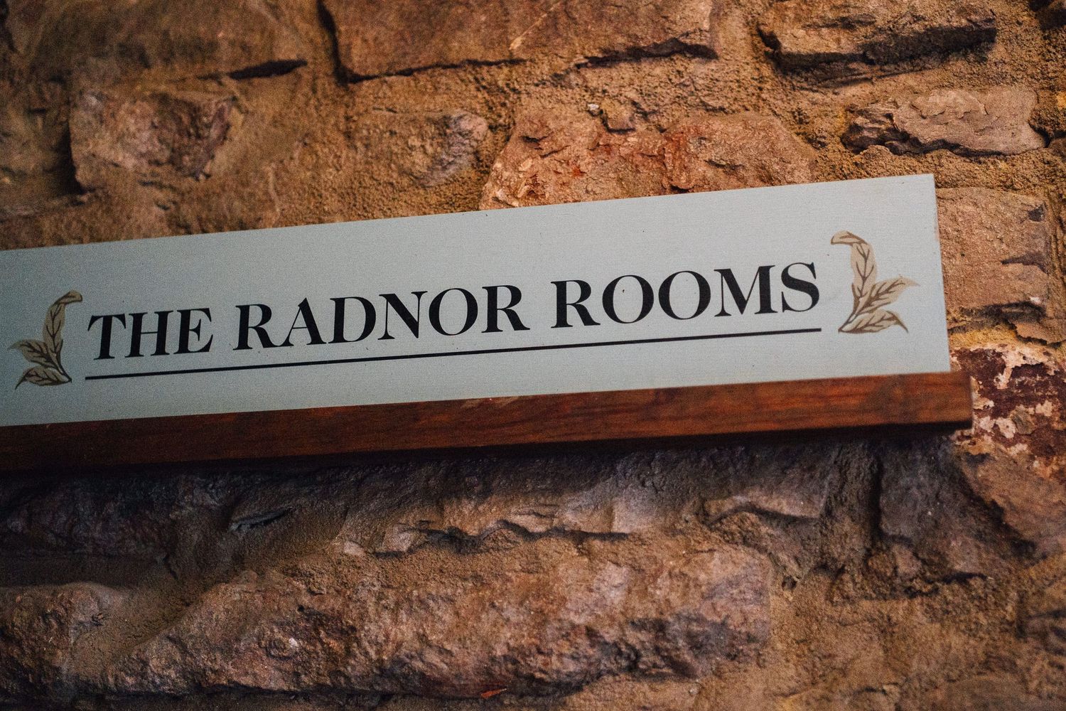 Rustic stone wall with wooden beams and vintage sign reading 'The Radnor Rooms' mounted at the top.