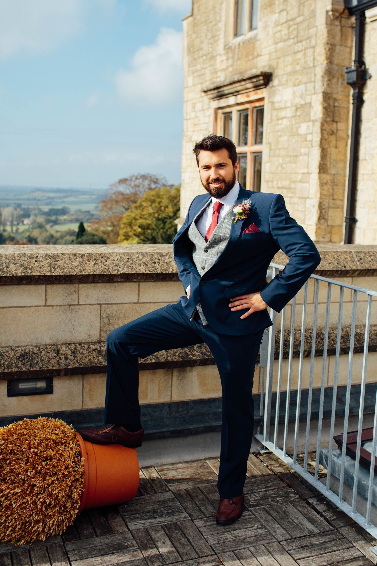 A series of photos showing someone in a navy suit posing casually against a stone balcony with scenic countryside views.