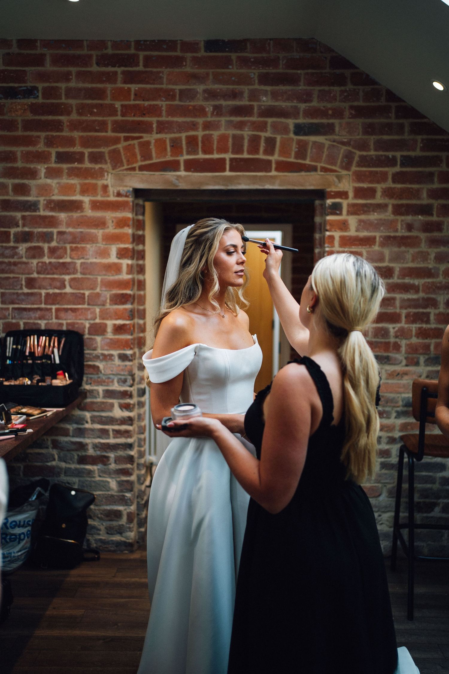 Two women in black and white dresses chat in front of exposed brick walls in a dimly lit space.