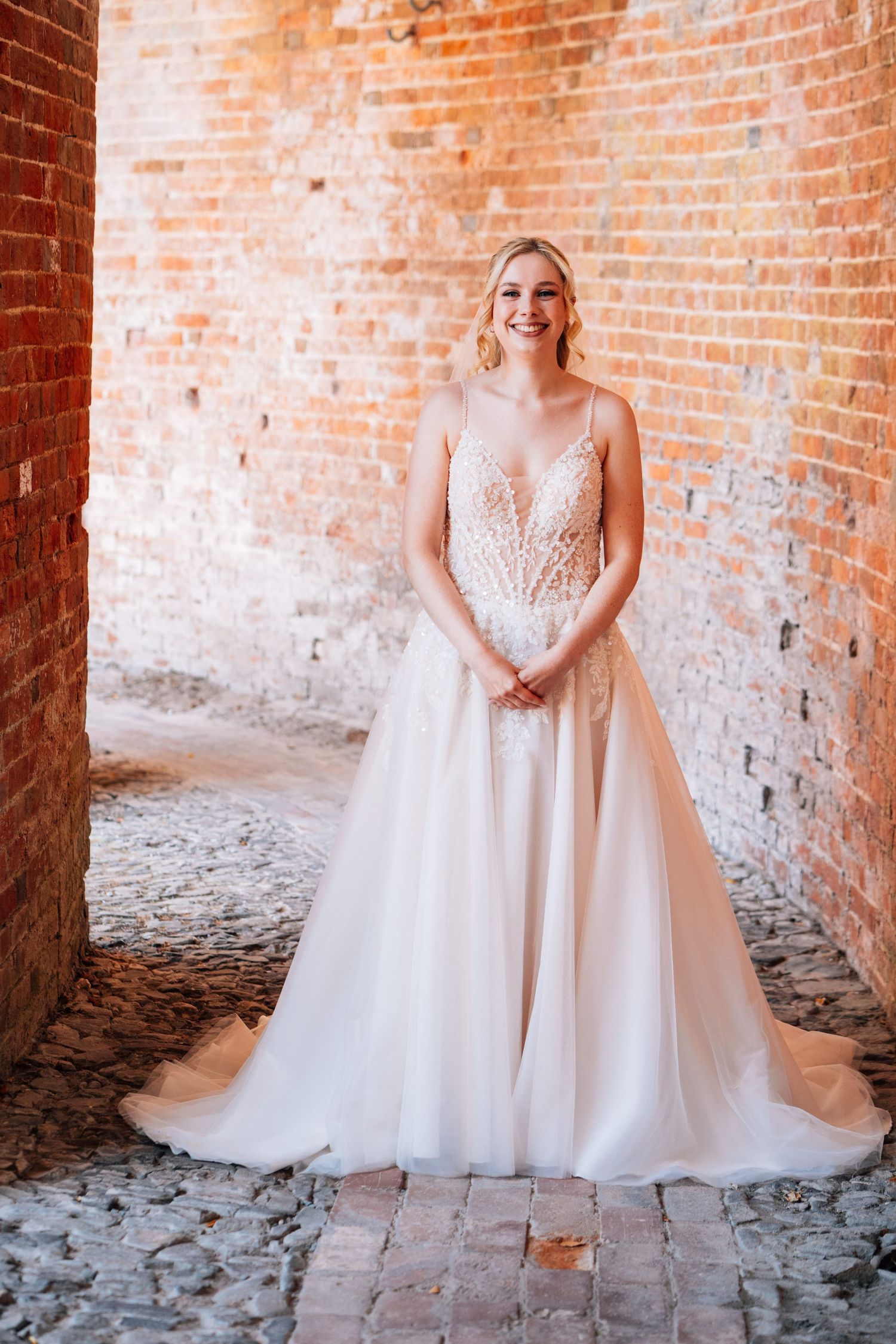 A stunning white ballgown wedding dress with lace bodice and tulle skirt photographed against rustic brick walls.