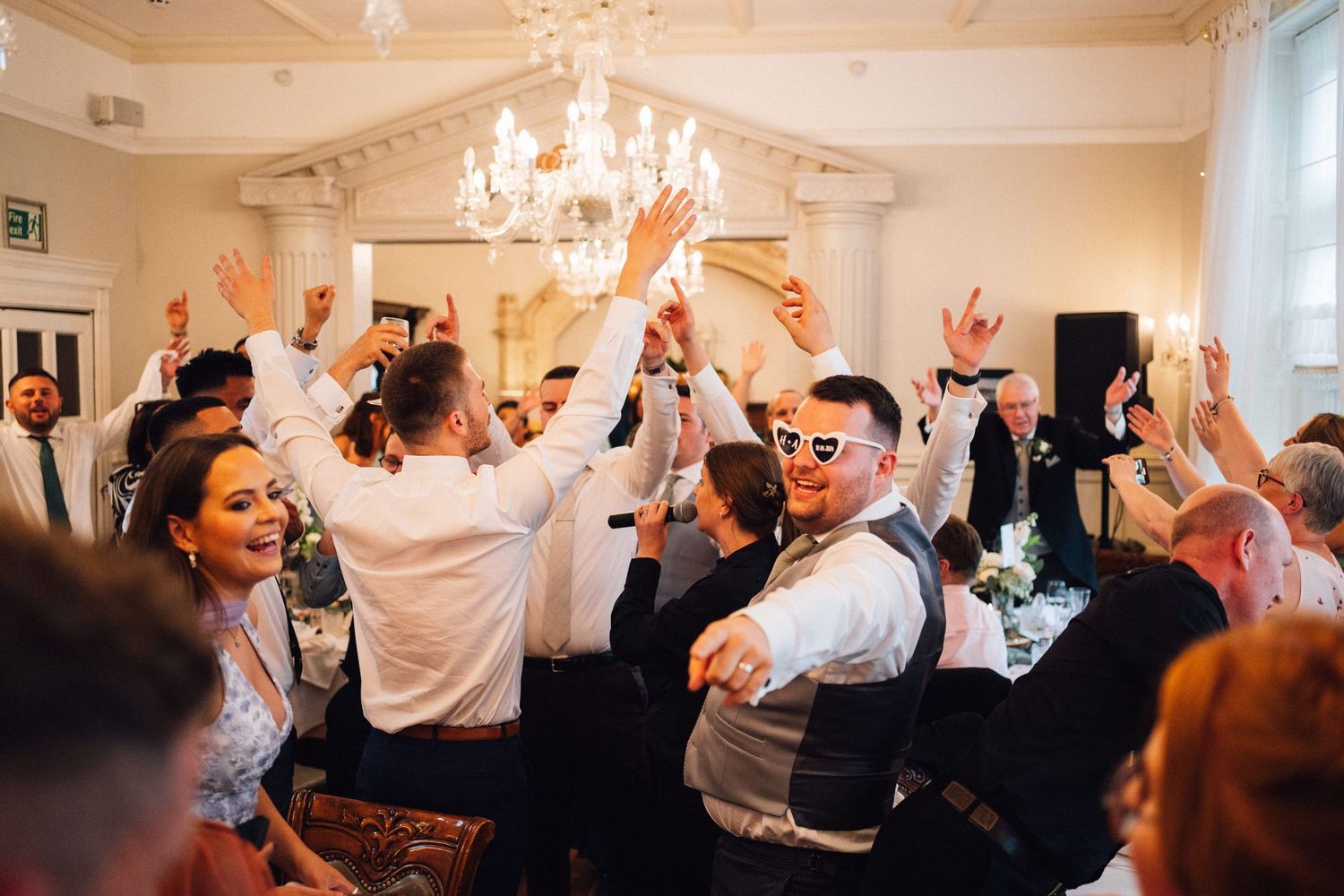 Wedding reception guests dancing and celebrating in an elegant ballroom with chandeliers.
