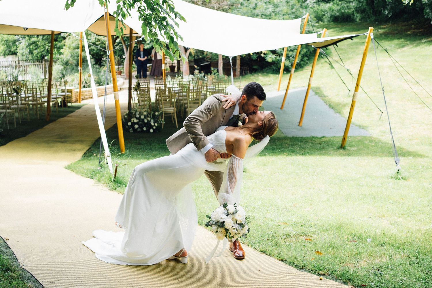 A romantic moment under a white canopy tent decorated with lights in an outdoor garden setting.