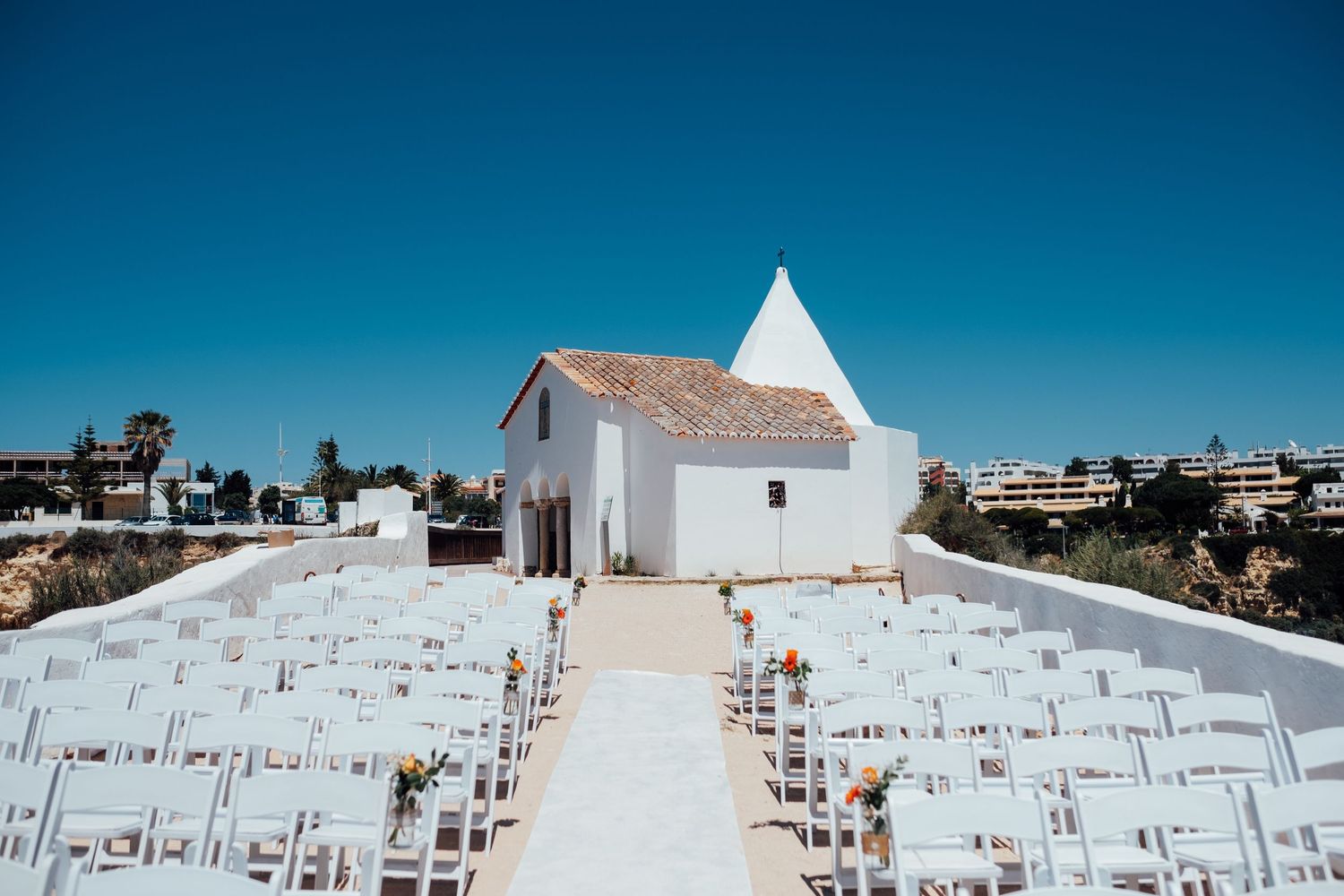 White chairs arranged for outdoor wedding ceremony against bright blue sky.