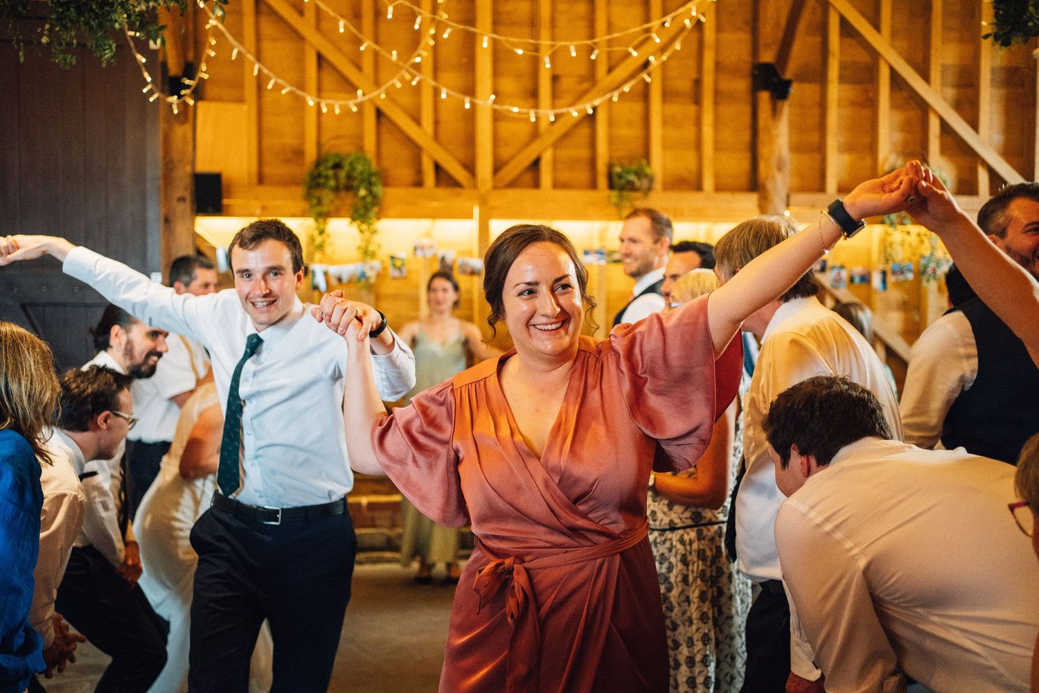 Wedding guests dancing and celebrating in a warmly lit rustic barn setting.