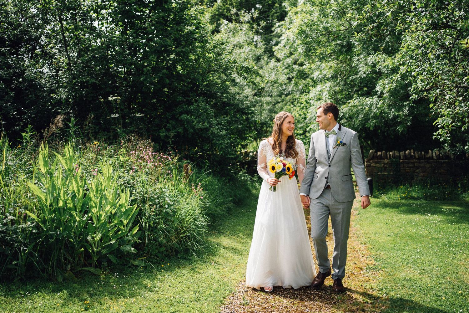 Bride and groom walking hand in hand through lush green garden on their wedding day.