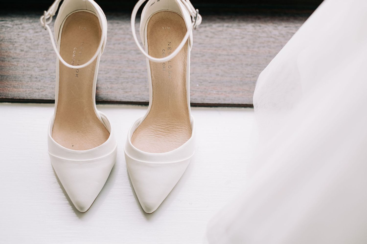 Elegant white bridal shoes arranged on a neutral gray background.