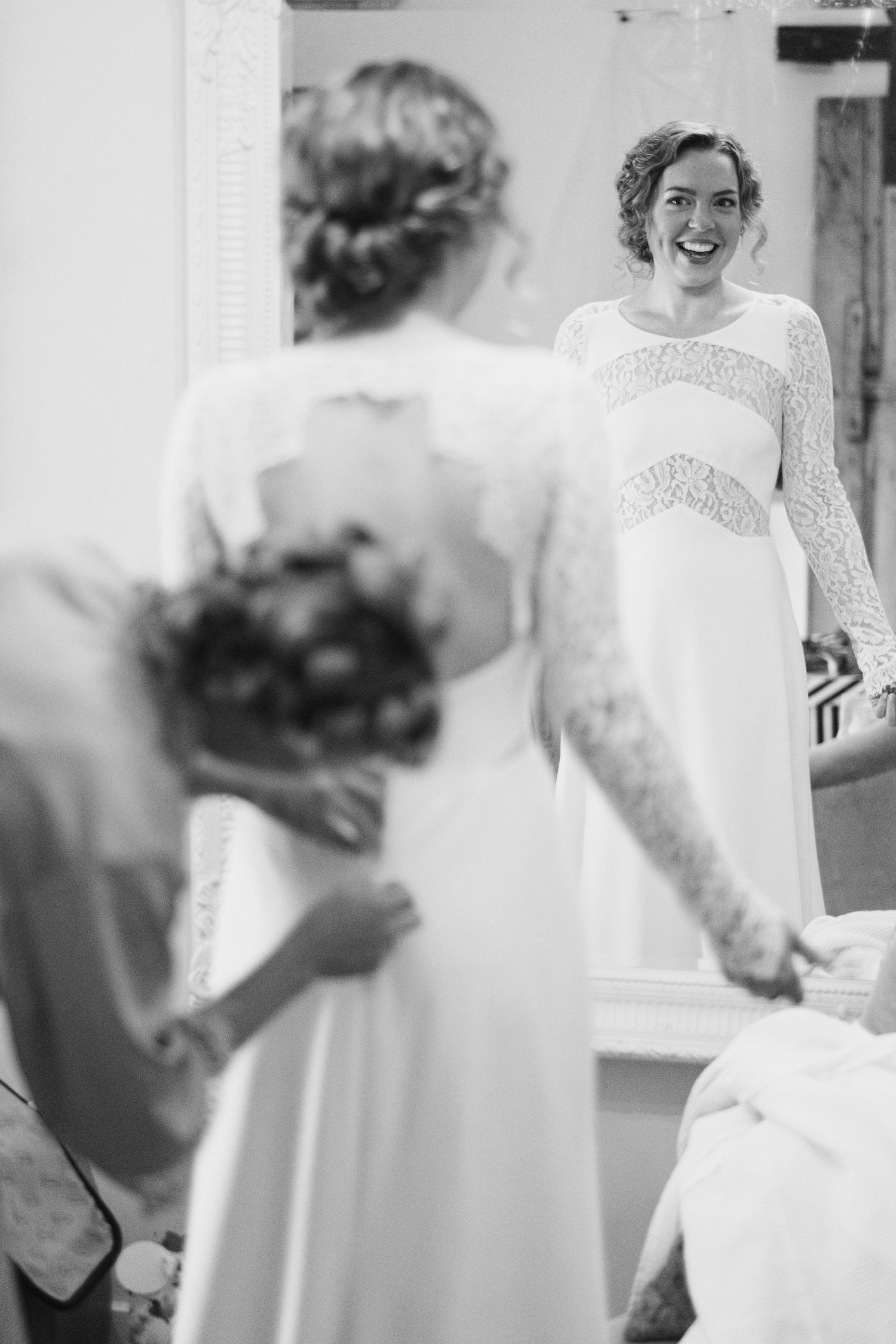 Candid black and white photograph capturing a joyful bridal moment in front of a mirror.