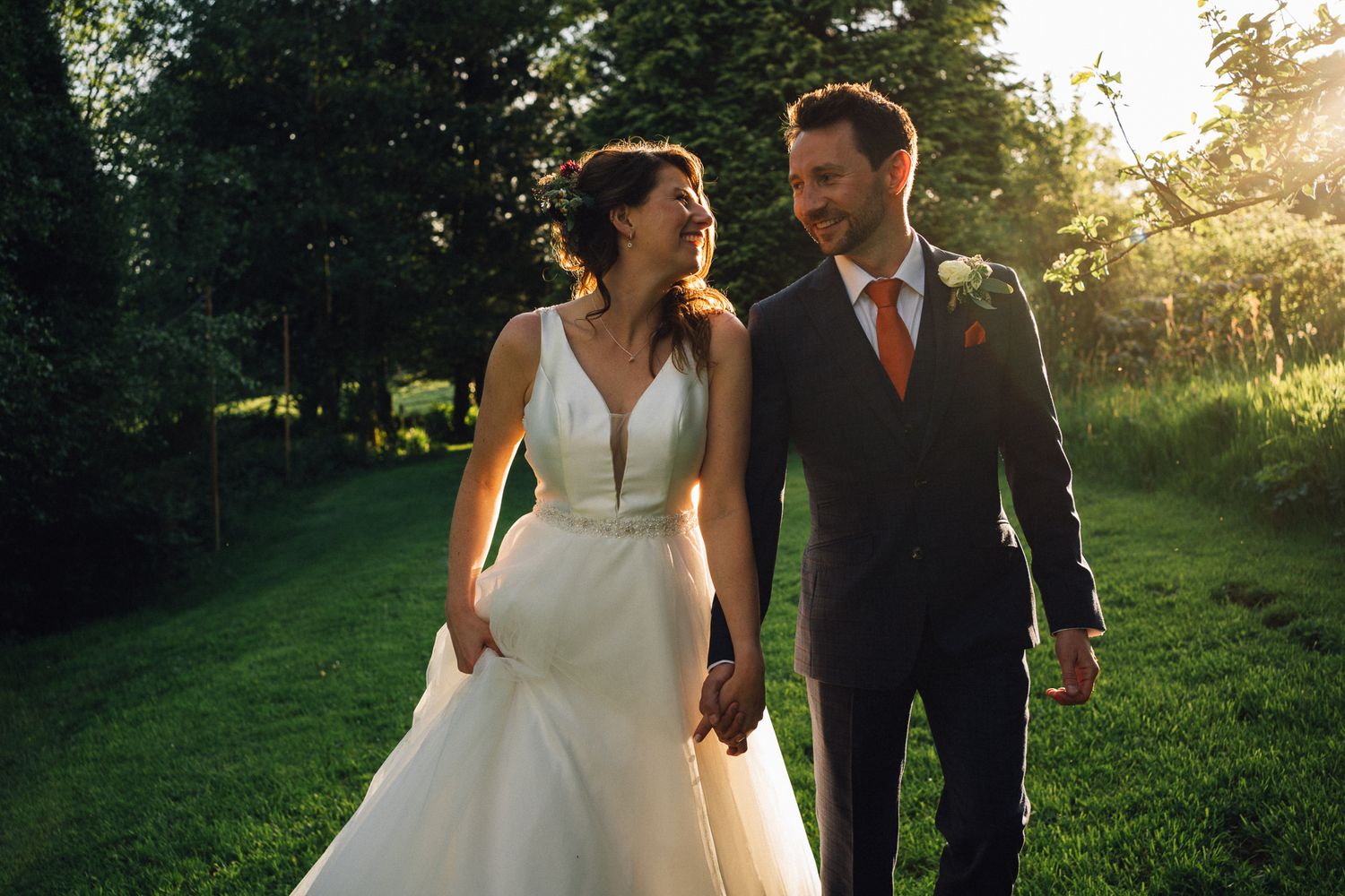 Newlyweds strolling through a sunlit garden path in formal attire.