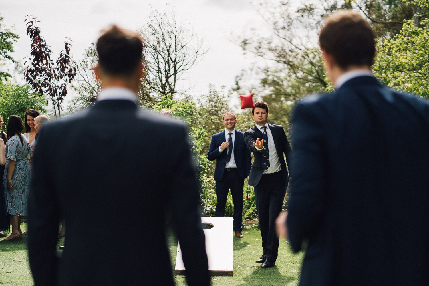 Groomsmen in dark suits stand in formation at outdoor wedding ceremony.