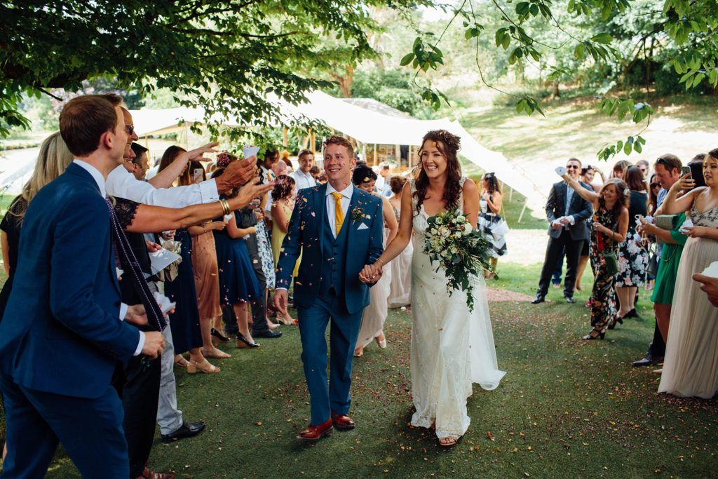 Wedding guests gather outdoors under trees for a celebration ceremony.