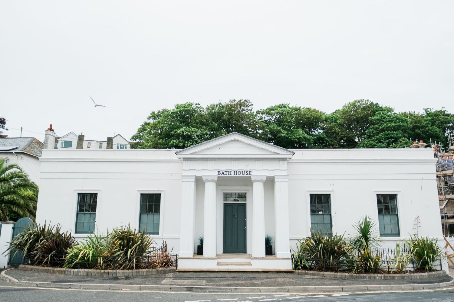 White neoclassical building with columns and symmetrical windows against cloudy sky.