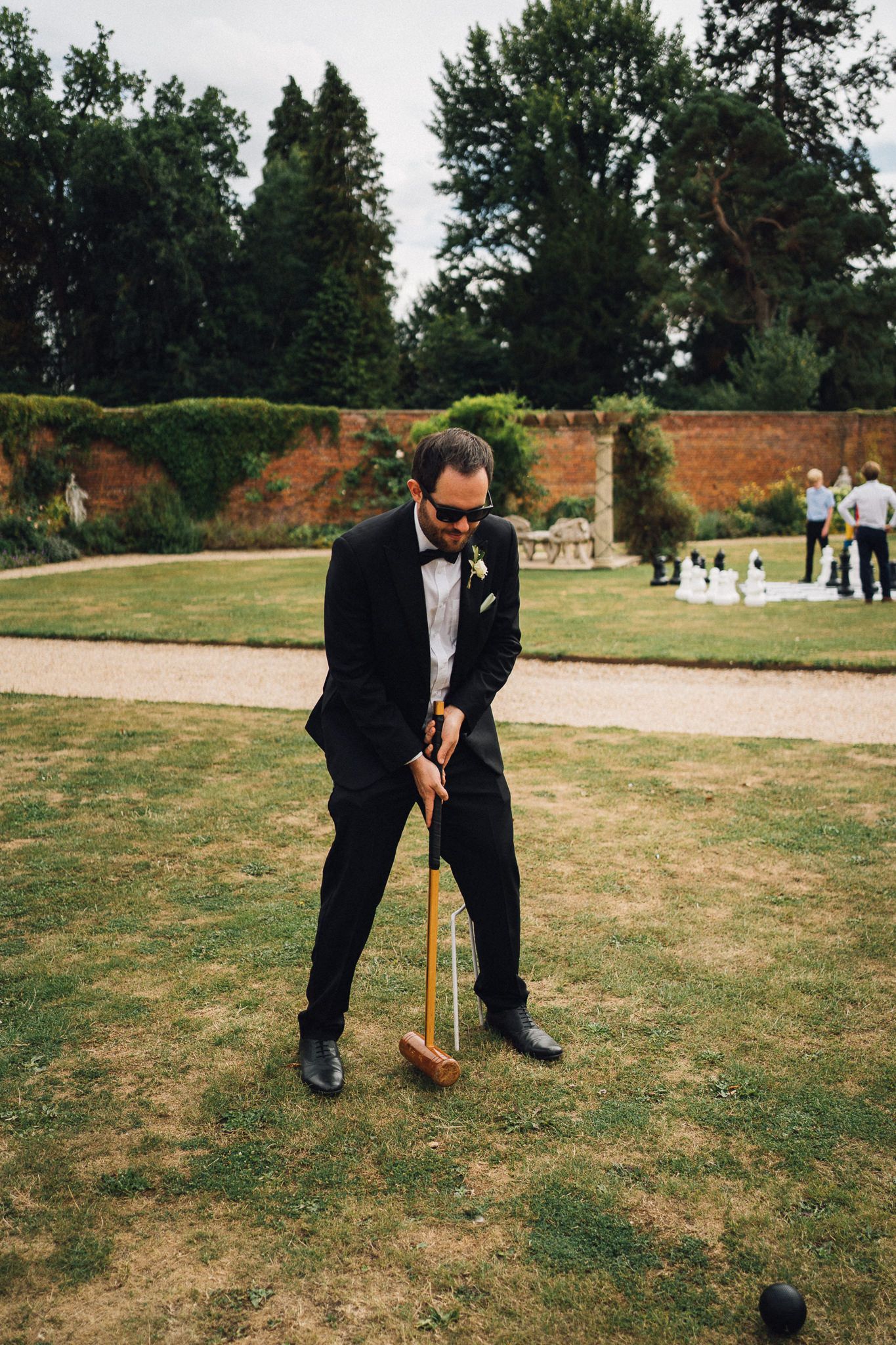 Person in formal suit playing croquet on grass during wedding festivities.
