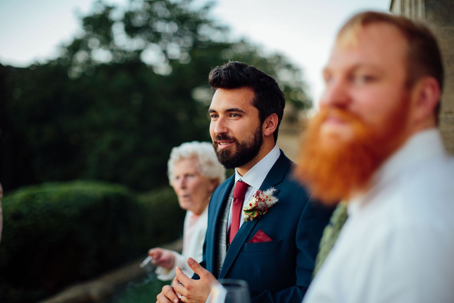 Wedding party members in formal attire standing outside historic stone building.